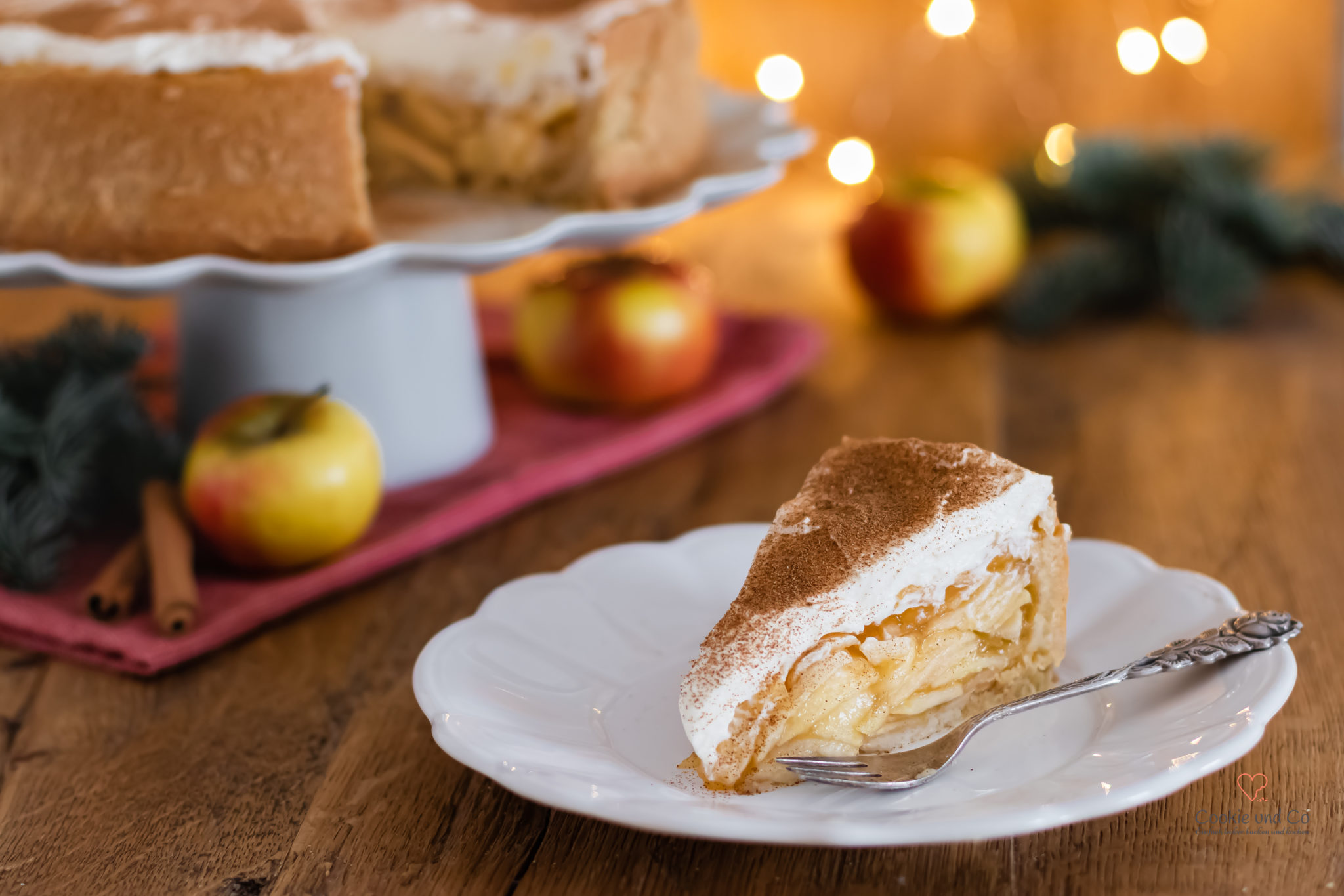 Ein Kuchenstück von einer Apfel-Glögg-Torte auf einem Teller mit weihnachtlicher Deko im Hintergrund.