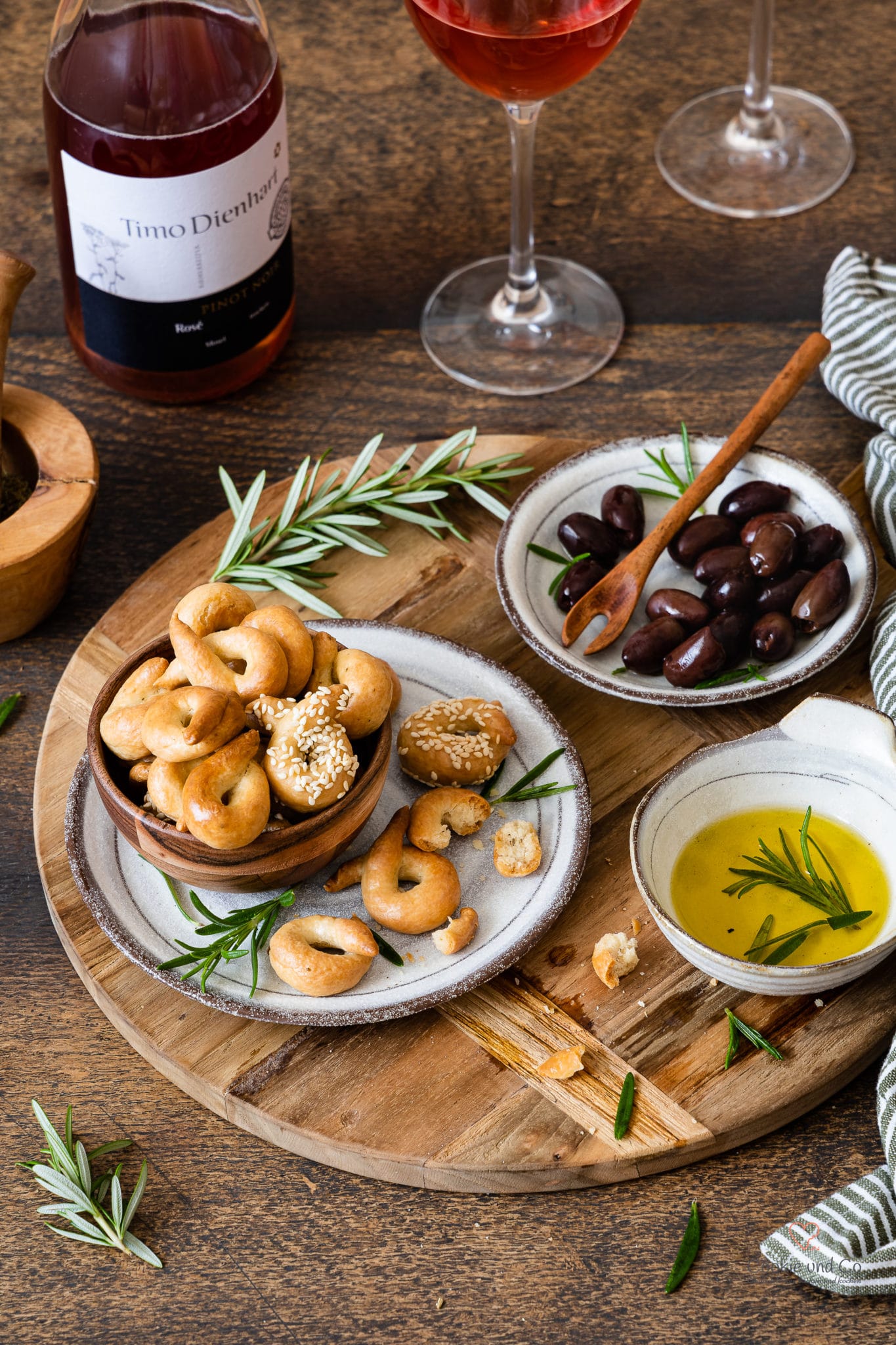 Taralli – ein italienisches Knabbergebäck auf einem Teller mit Olivenöl, Oliven, Rosmarin und Wein im Hinte