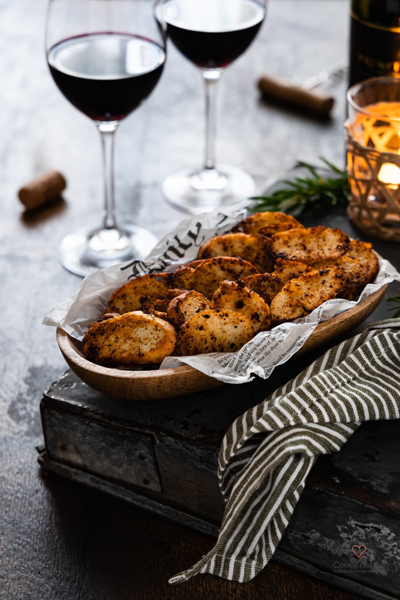 Brotchips in einer Holzschale mit einer Kerze und Rotweingläsern im Hintergrund.