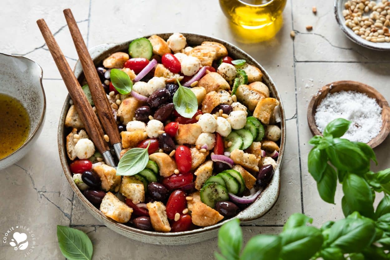 Italienischer Brotsalat „Panzanella“ in einer Salatschüssel mit Basilikum im Vordergrund.